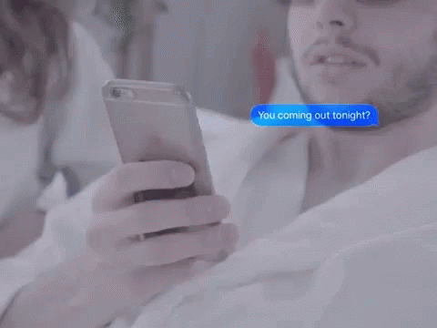 two men in bed texting on their phones