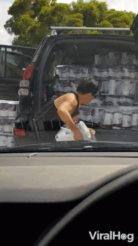 a woman bending over while putting packages in the back of a car