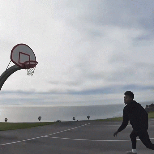 man on asphalt playing with basketball hoop in large empty lot