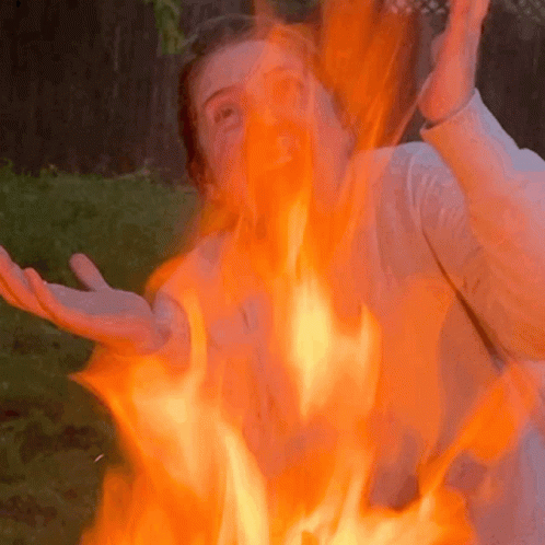 a woman smiles at the camera with arms outstretched as the woman plays in a fire