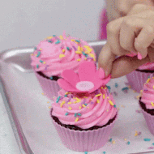 a hand is picking up a blue cupcake off a plate