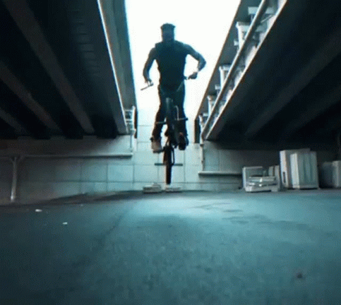 man rides his bike on a city street underneath a bridge