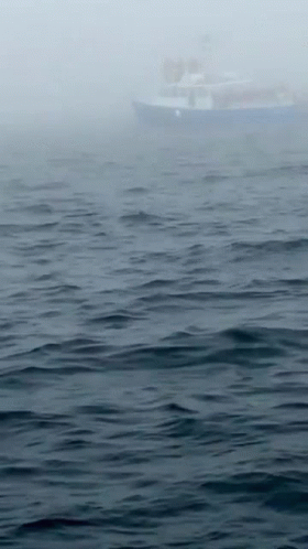 the sky is very foggy as a boat sails on the water