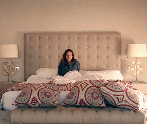 a woman is sitting on a large bed with pillows and blankets