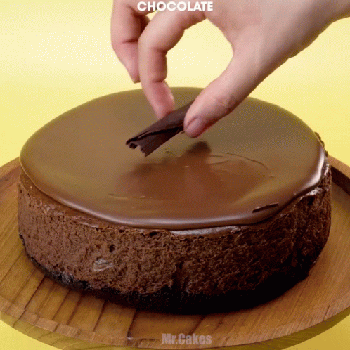 someone decorating a chocolate cake on top of a wooden tray