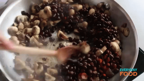 a large bucket of blue and black seeds with one spoon in it