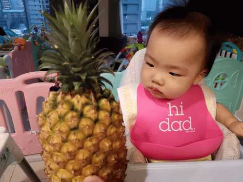 a baby sitting in a high chair next to a pineapple
