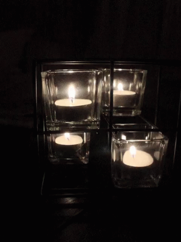 four candles floating in dark water inside square containers