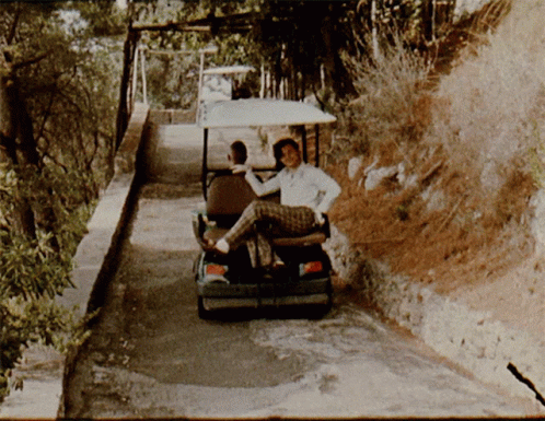 a golf cart with two people on it pulling a cart full of luggage