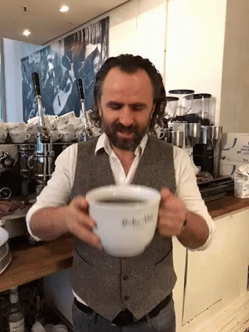 a man holds a small coffee cup and makes a strange face