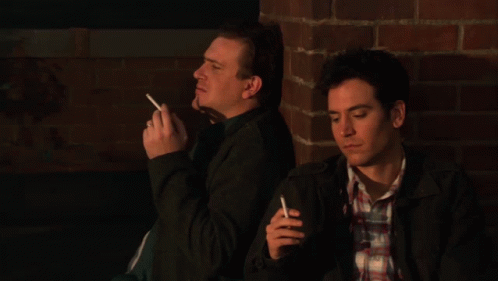 a couple of men standing in front of a brick wall smoking