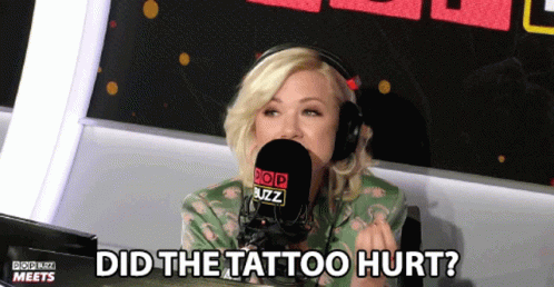 woman with pale hair and blue eyes sits in a chair next to a microphone with a caption that reads did the tattoo hurt?