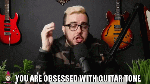 a man in glasses sitting at a table in front of guitars