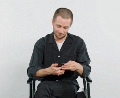 a man sitting in a chair while holding a cell phone