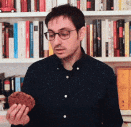 man in glasses is holding a cellphone next to book shelves