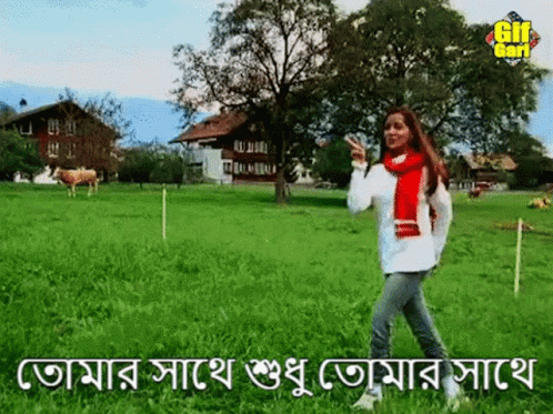 an indian woman in a grassy field with a tree and buildings behind her