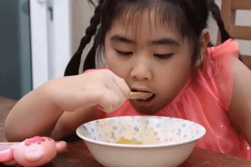 a girl wearing purple and eating from a bowl
