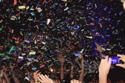 a large crowd is gathering with their hands in the air and confetti falling off of them