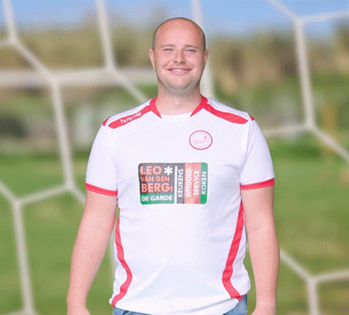 a smiling man stands in front of a soccer net