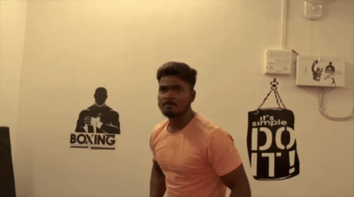 man in gym t - shirt staring at camera with boxing logo on wall behind him
