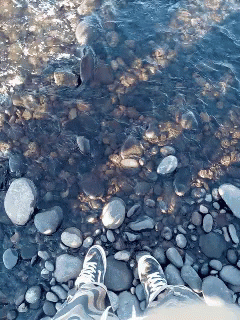 a person's feet standing on rocks and water
