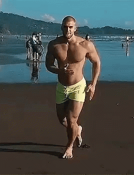man wearing green trunks running on sandy beach near water