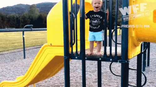 a toddler stands at a playground while a view of water is in the background