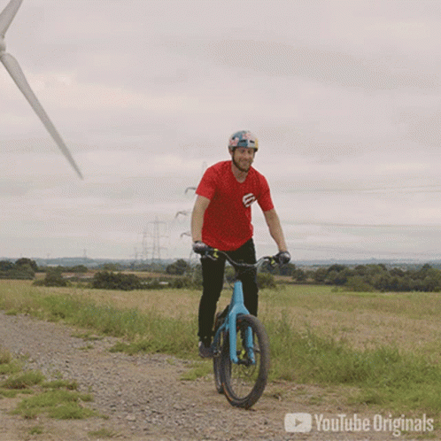 a man riding his bike down the road in front of wind turbines