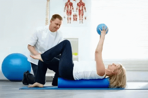 two people sitting on exercise mats while one man is holding a ball