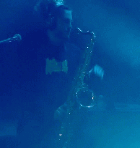 a man with a microphone behind him plays on a saxophone
