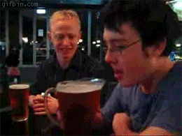 two men laughing while drinking some beer at the bar