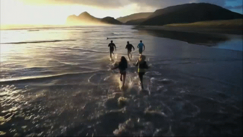 four people walk on the beach holding surfboards