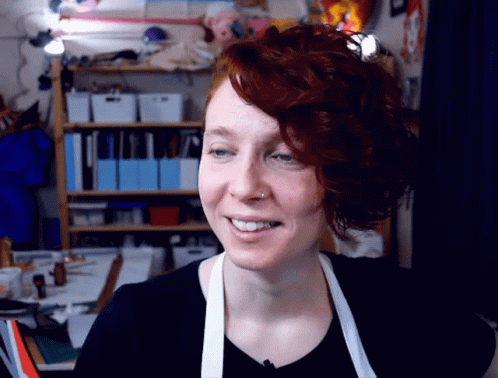 a smiling woman in an apron in a room full of clutter