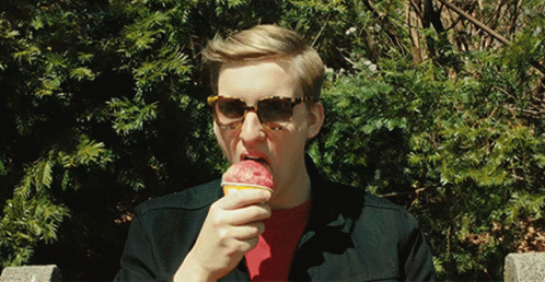 a man in sunglasses eats a purple doughnut