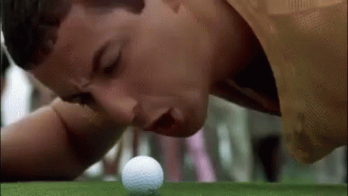 a man bending over looking at a golf ball on the green