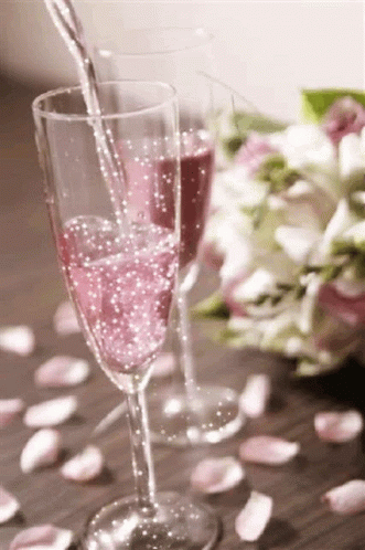 two champagne glasses next to each other and pink flowers