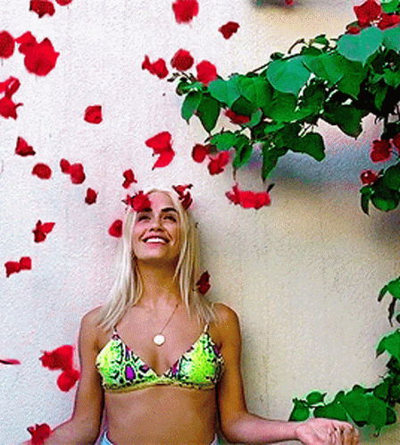 woman in pink and green bikini standing with flowers on wall