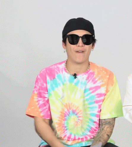 a man with glasses and tie dye shirt is wearing a black hat