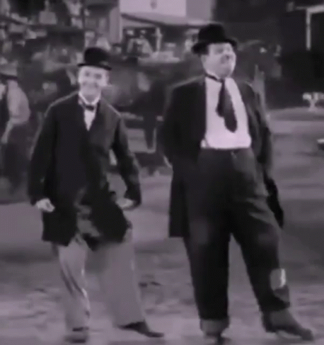 two men are walking down the street wearing hats and tails