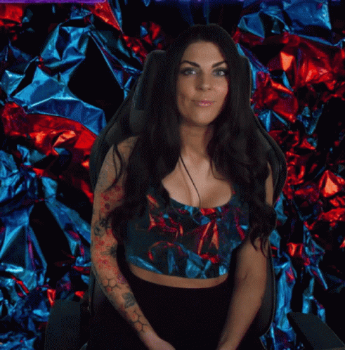 a woman with tattoos on her arms poses in front of a wall of foil