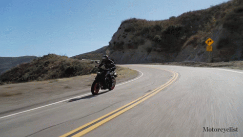 a motorcycle riding down the road near a hill