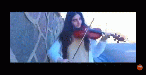 a woman playing violin while standing against a wall