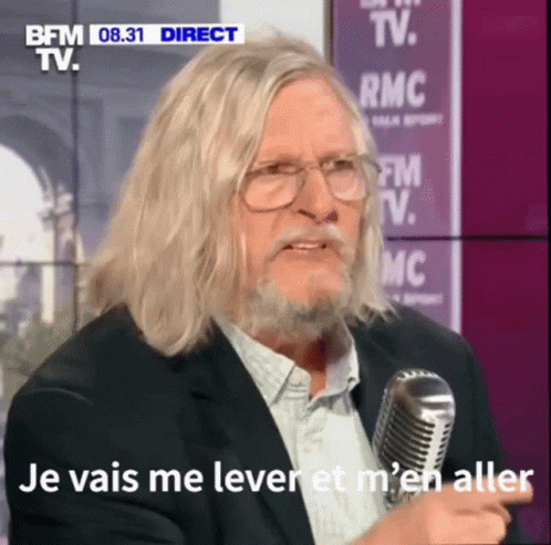 a man with long white hair is talking into a microphone