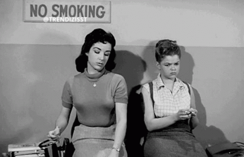 two women smoking cigarettes sitting on the bed