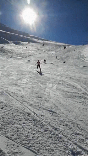 skiers are coming down a snowy slope under the sun