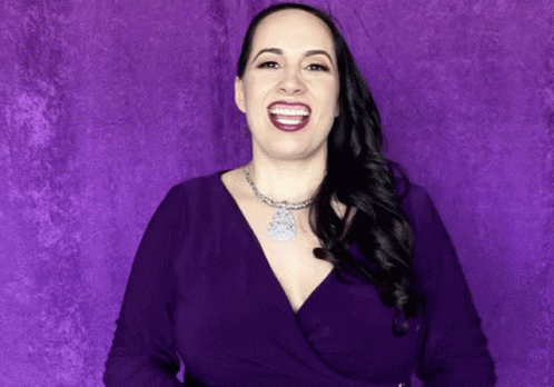 a woman in dark purple is smiling and has one eye open