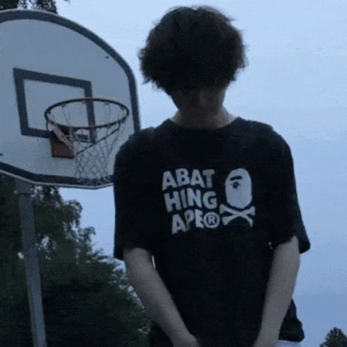 a person in an abat hip shirt stands in front of a basketball hoop