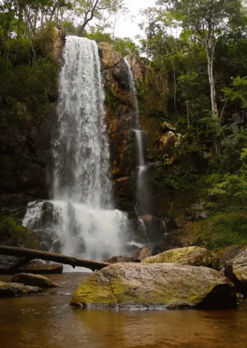 large waterfall with a body of water next to rocks and trees
