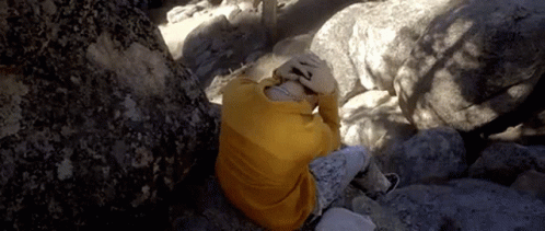 a person wrapped up with blankets looking up while climbing through some rocks