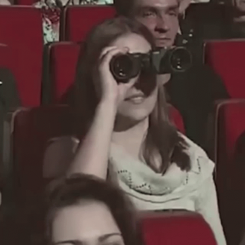 people sitting in an auditorium looking through binoculars